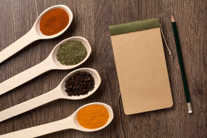 notebook and pencil for recipes and spices in spoons on wooden t